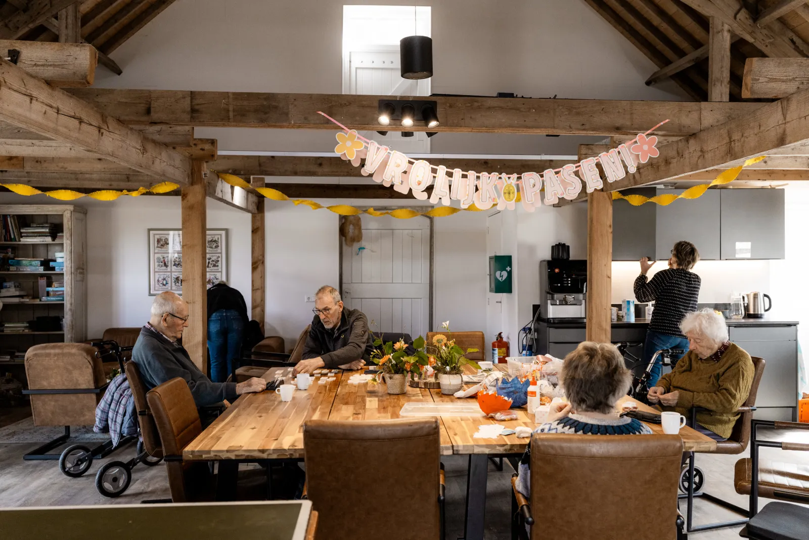 Aan een grote tafelen zijn ouderen creatief bezig en spelletjes aan het spelen.