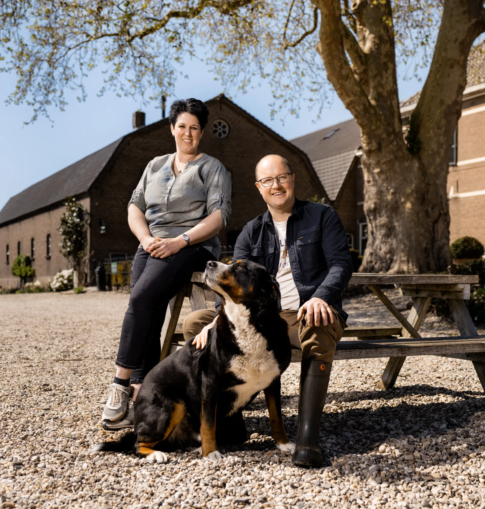 Emiel en Esther, eigenaars van Hof zum Walde, op een picnicbankje met hun hond erbij.